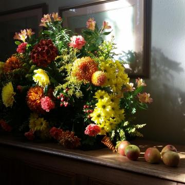 A flower arrangement with some apples beside it
